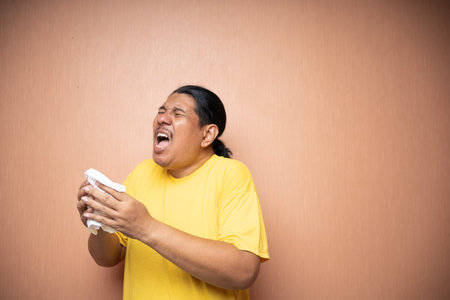 old asian man wearing yellow tshirt using tissue to cover sneezing in plain background isolated