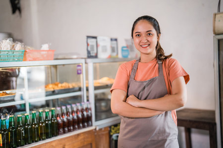 Attractive female shop owner wearing apron with crossed hands standing at food stall