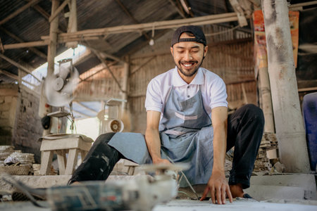 Male stone craftsman sits while measuring and using grinding tools to shape stones in the workshopの写真素材