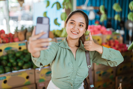 female customer standing with thumb up while taking selfie photo at the fruits shopの写真素材