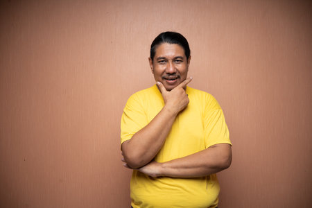 old asian man feeling confident with folded hand and touching his chin in plain background isolatedの写真素材