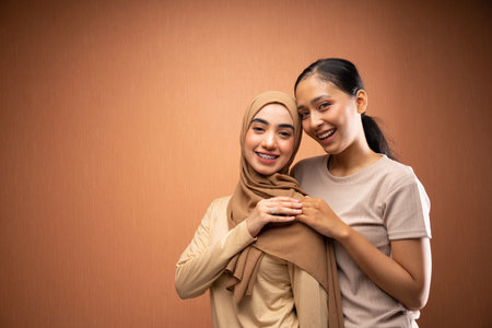 happy women hijab and no hijab wearing cream t-shirt hugging each other and smiling in orange backgroundの写真素材