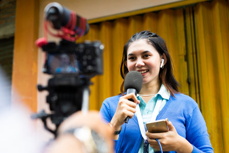 a female reporter in blue cardigan talking to the camera during video shooting for news materialの写真素材
