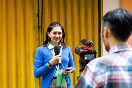 a beautiful reporter in blue cardigan and the cameramen recording videos for news material using one set of camera and a black microphoneの写真素材