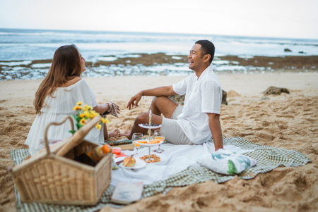 newlywed couple sitting on a picnic blanket chatting during a picnic at the beachの写真素材