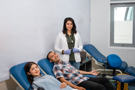 smiling female doctor standing next to two patients during blood transfusion in hospital roomの写真素材