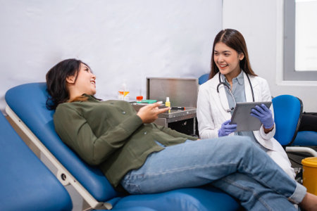 female patient lying down during consultation with seated female doctor carrying a digital tablet at hospitalの写真素材