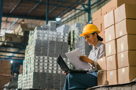 female factory worker sits using a laptop computer while working in a factoryの写真素材