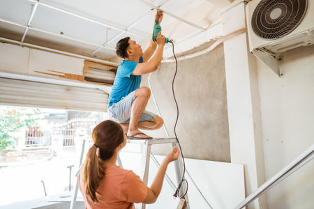 husband and wife work together to install a ceiling frame using a drill during home renovationsの写真素材