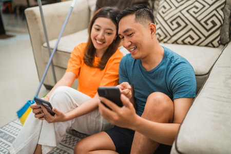 asian couple watch something on the phone after cleaning the houseの写真素材