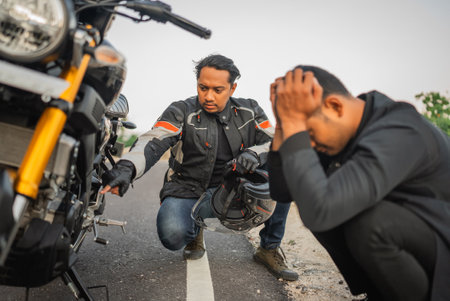 asian rider checking broken motorbike that belongs to his friendの写真素材