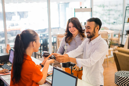 smiling Asian man using EDC device while buying and making payment at the store counterの写真素材