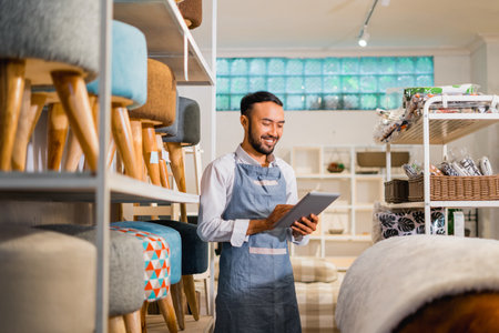 shopkeeper man in apron using a tablet while standing in a furniture storeの写真素材