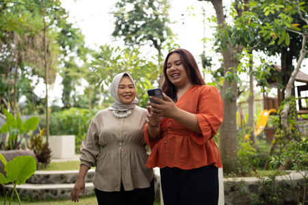 businesswoman holding and showing her phone to hijab coworker in happy expression
