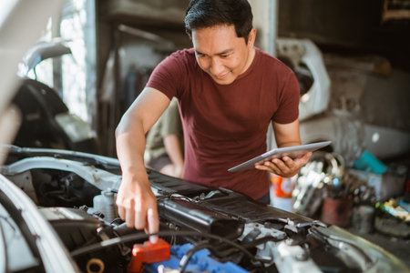 young male mechanic wiring a battery while using a digital tablet at a repair shopの写真素材