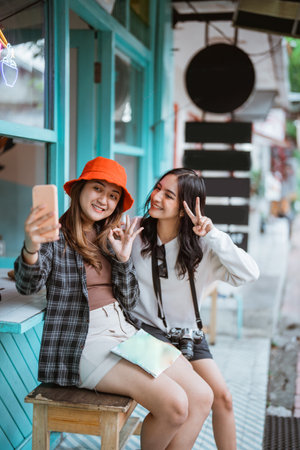 two Asian girls make a video call using a cell phone while sitting at restの写真素材