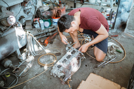 male mechanic cleaning a cylinder head using a duster gun while repairing an engine in a workshopの写真素材