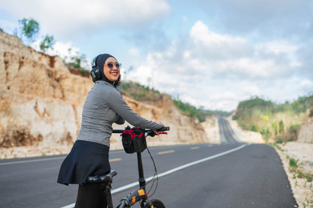 female athlete wearing hijab listening music during biking exerciseの写真素材