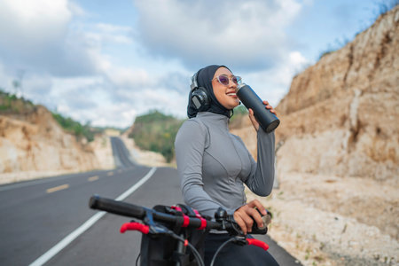 hijab woman enjoying drinking water when biking outdoorsの写真素材