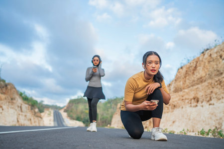 athletic woman in squat position using phone, her hijab friend standing behind her