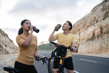 female and male biker taking rest from biking and drinking waterの写真素材