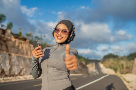 sporty hijab woman using phone with thumb up gesture, working out outdoor, jogging conceptの写真素材