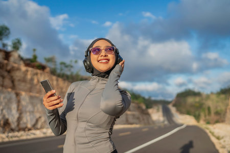 smiling hijab woman wearing sportswear using phone and earphone for listening to music