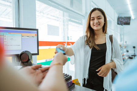 Asian woman gives credit card to shopkeeper for payment while at minimarket store cashierの写真素材