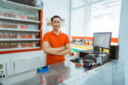 male shop assistant smiling at the camera with his arms crossed standing at the cashier