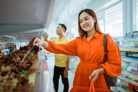 young woman picks up items on a shelf while carrying a shopping cart in a supermarketの写真素材