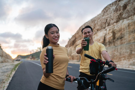 happy athletic biker couple holding bottle, taking rest from biking