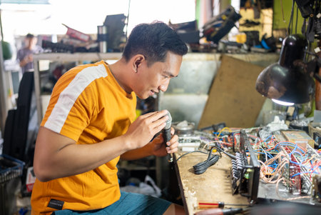 Male technician checks microphone while repairing amplifier in electronics repair roomの写真素材