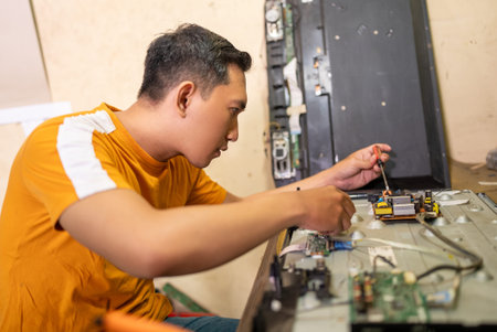 male technician using screwdriver while removing bolts of led tv electronic components on workbench
