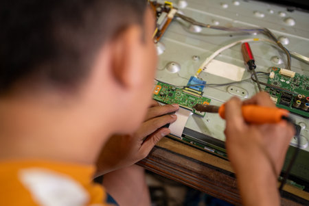 technician man uses soldering iron to replace electronic component circuit of led tv at service stationの写真素材