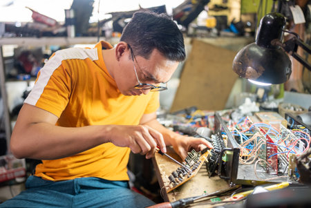bespectacled repairman repairing an electronic circuit using a screwdriver on a workbench