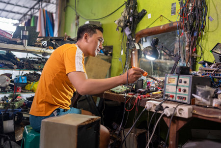 Asian male technician using soldering iron while repairing an electronic circuit at a service stationの写真素材