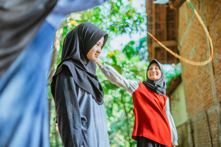 close up view hijab girl playing rope skipping outside the house with her friendsの写真素材
