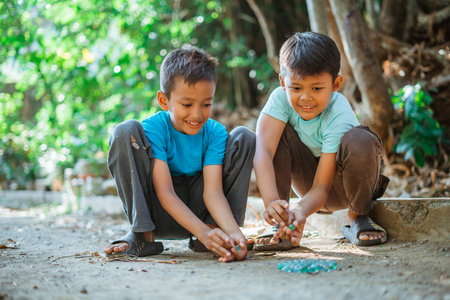asian boys hitting marbles using hand on their playtimeの写真素材