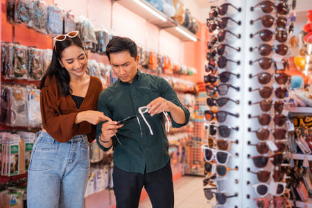 confused man holds two glasses while choosing with his girlfriend at an accessories storeの写真素材