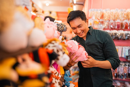 handsome young man smiles at a doll while choosing it for a gift at an accessories storeの写真素材