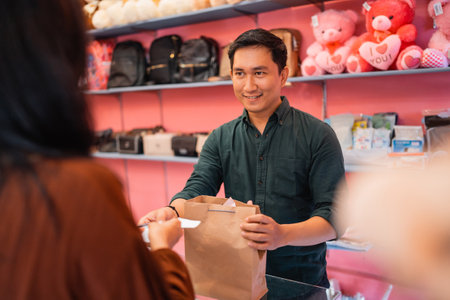 male waiter smiling while serving customers and handing over shopping items at the checkout counterの写真素材