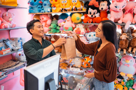 handsome male waiter giving paper bag to buyer woman while shopping in accessories storeの写真素材