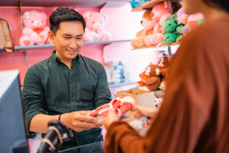 young Asian man receives customer shopping item when customer is going to pay in accessories store