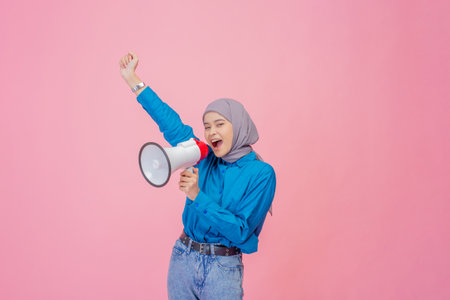 A vibrant young woman excitedly uses a megaphone against a bright pink backgroundの写真素材