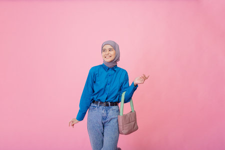 A stylish young woman poses confidently with a handbag in front of a pink backdrop.の写真素材