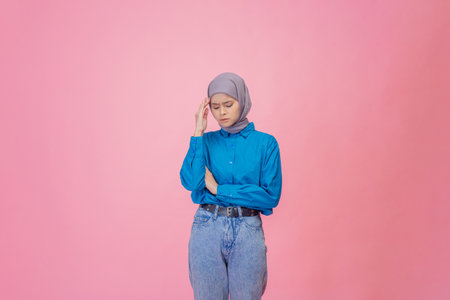A young woman in a blue shirt and gray hijab strikes a thoughtful pose, reflecting deeplyの写真素材