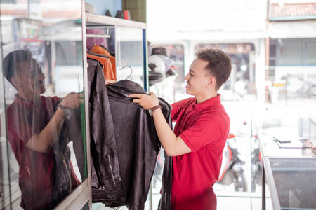 side view picture of male employee in red polo shirt arrange black leather jacket on shelfの写真素材