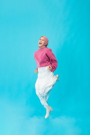 A joyful woman in a colorful outfit jumps against a blue backdrop, showcasing energy