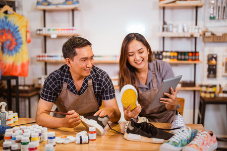 Man and woman holding tablet and sneakers shoes painting at workshop