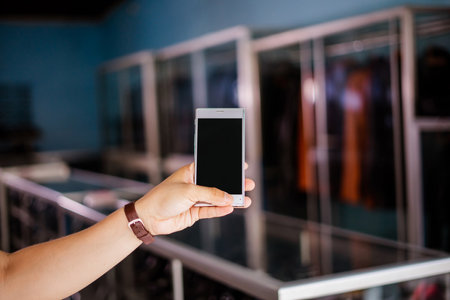 blurred and cropped view of hand holding phone with blank screen at leather shoes storeの写真素材
